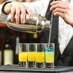 Barman en gilet versant un cocktail depuis un shaker dans quatre verres à shot longs
