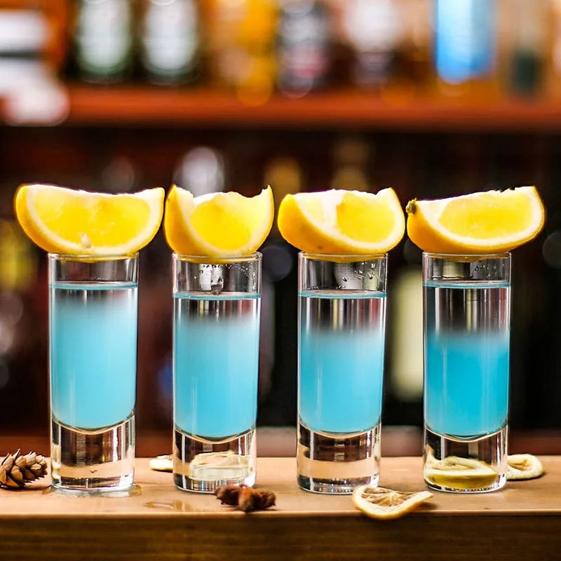 Quatre verres à shot longs remplis d'un cocktail bleu et garnis de quartiers de citron
