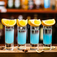 Quatre verres à shot longs remplis d'un cocktail bleu et garnis de quartiers de citron