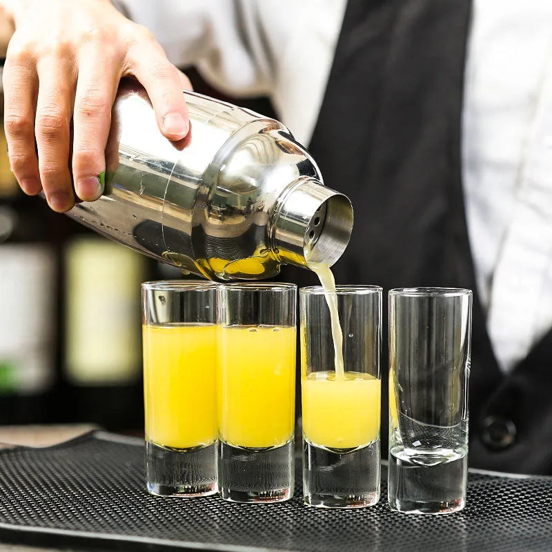 Gros plan sur un shaker versant du jus d'orange dans des verres à shot longs alignés