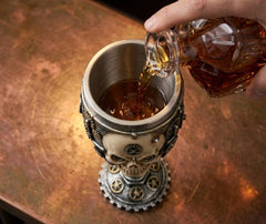 Verre à vin tête de mort rempli d'une boisson ambrée versée depuis une carafe en cristal