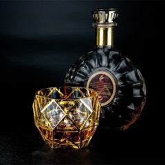 Verre à whisky de luxe posé à côté d'une bouteille de cognac Rémy Martin sur fond noir