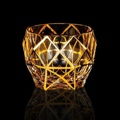 Verre à whisky de luxe vide au design géométrique doré, photographié sur fond noir avec reflet