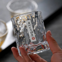 Gros plan sur la texture martelée du verre à whisky japonais tenu en main, avec son étiquette artisanale japonaise portant la mention verre fait main.