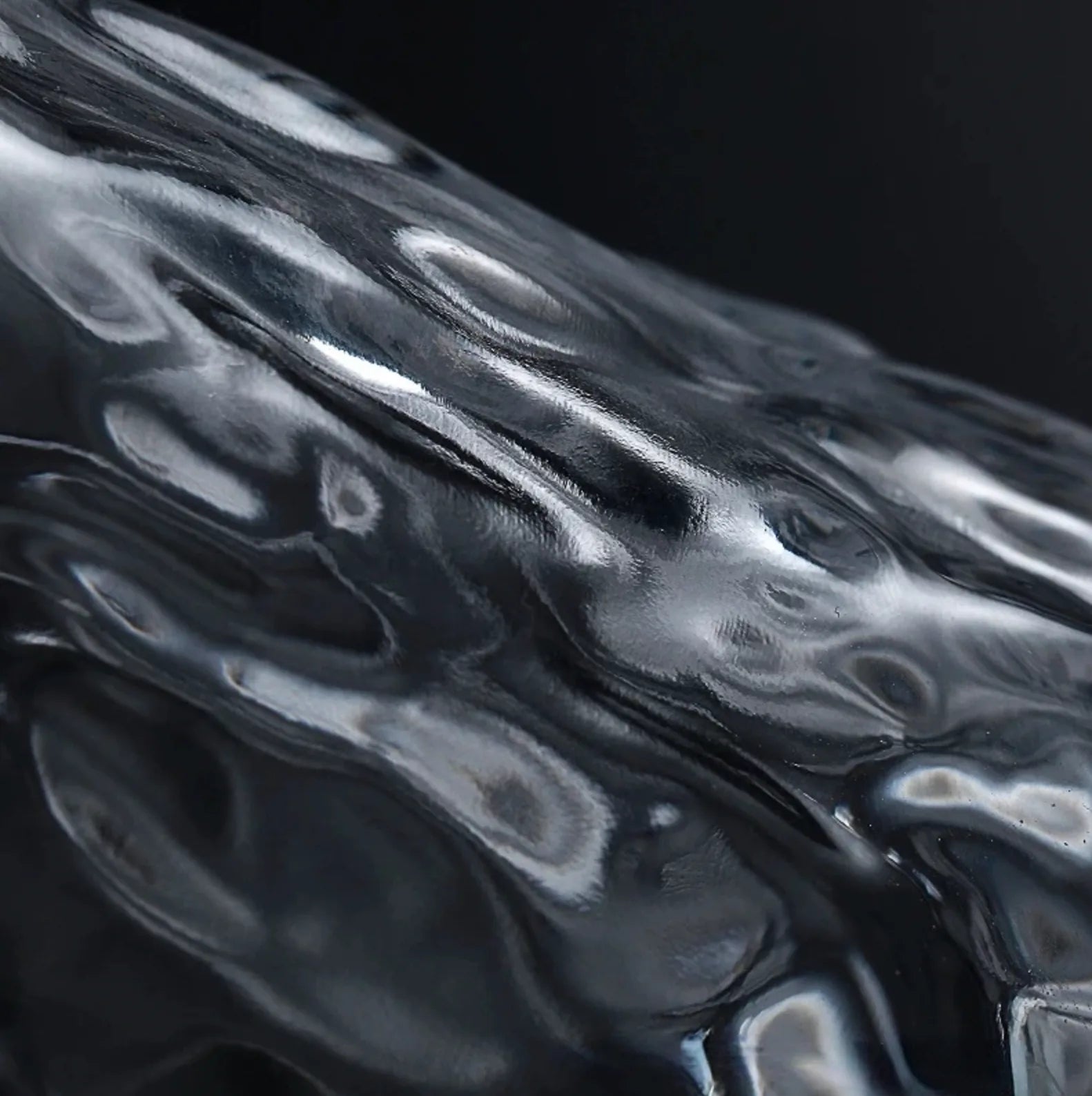 Macro extrême sur la paroi en verre martelé du verre à whisky japonais, texture ondulée et reflets sur fond sombre.