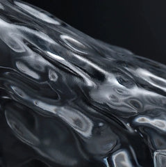 Macro extrême sur la paroi en verre martelé du verre à whisky japonais, texture ondulée et reflets sur fond sombre.