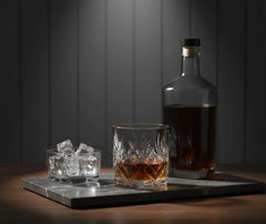 Verre à whisky vintage posé sur un plateau en marbre avec un bol de glaçons et une bouteille de whisky, ambiance bar tamisée.