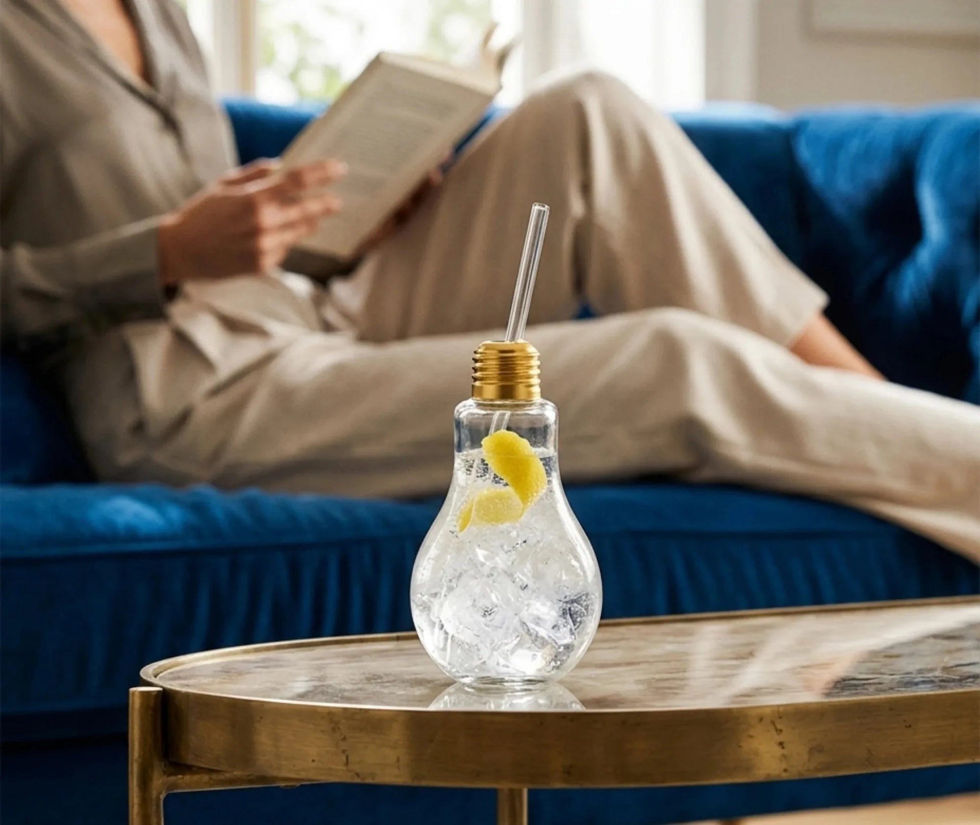 Verre ampoule à cocktail rempli de gin tonic glacé avec un zeste de citron, posé sur une table basse dorée dans un salon cosy.