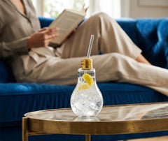 Verre ampoule à cocktail rempli de gin tonic glacé avec un zeste de citron, posé sur une table basse dorée dans un salon cosy.
