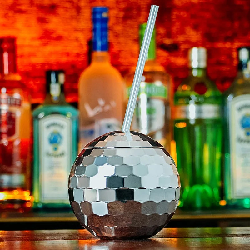 Verre à cocktail boule disco posé sur un comptoir de bar avec des bouteilles d'alcool floues en arrière-plan