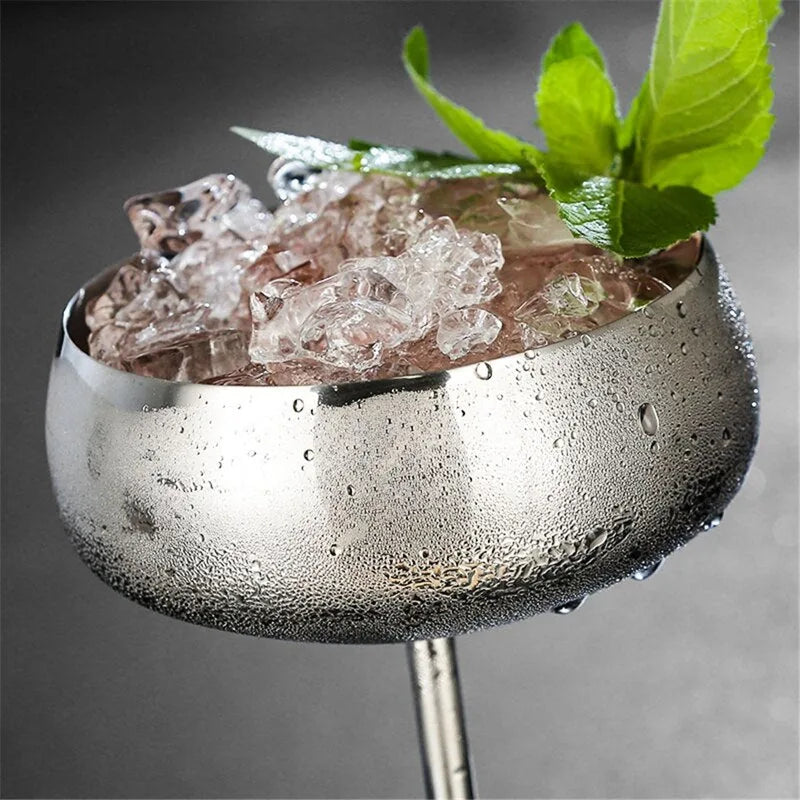 Gros plan sur le bord du verre coupe argenté rempli de glaçons et surmonté d'une feuille de menthe, avec des gouttes de condensation.