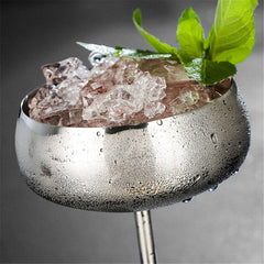Gros plan sur le bord du verre coupe argenté rempli de glaçons et surmonté d'une feuille de menthe, avec des gouttes de condensation.