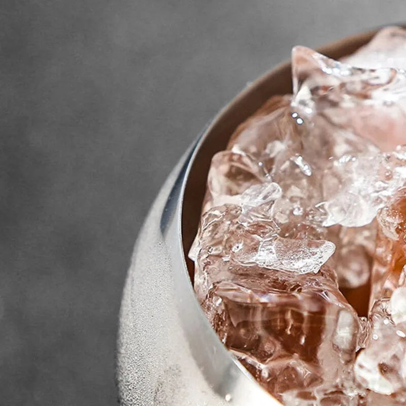 Macro photo des glaçons teintés de rose à l'intérieur du verre coupe, avec le bord métallique au premier plan.