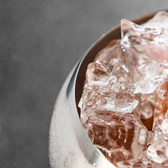 Macro photo des glaçons teintés de rose à l'intérieur du verre coupe, avec le bord métallique au premier plan.