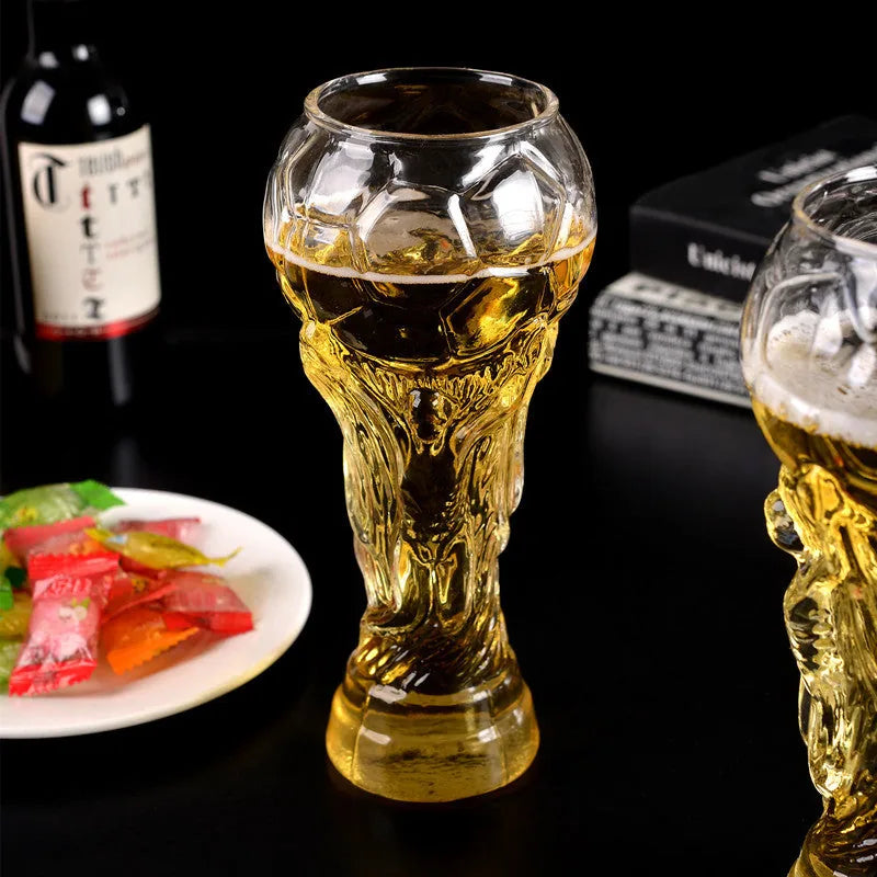 Deux verres Coupe du Monde remplis de bière ambrée sur une table noire avec bouteille de vin et amuse-bouches