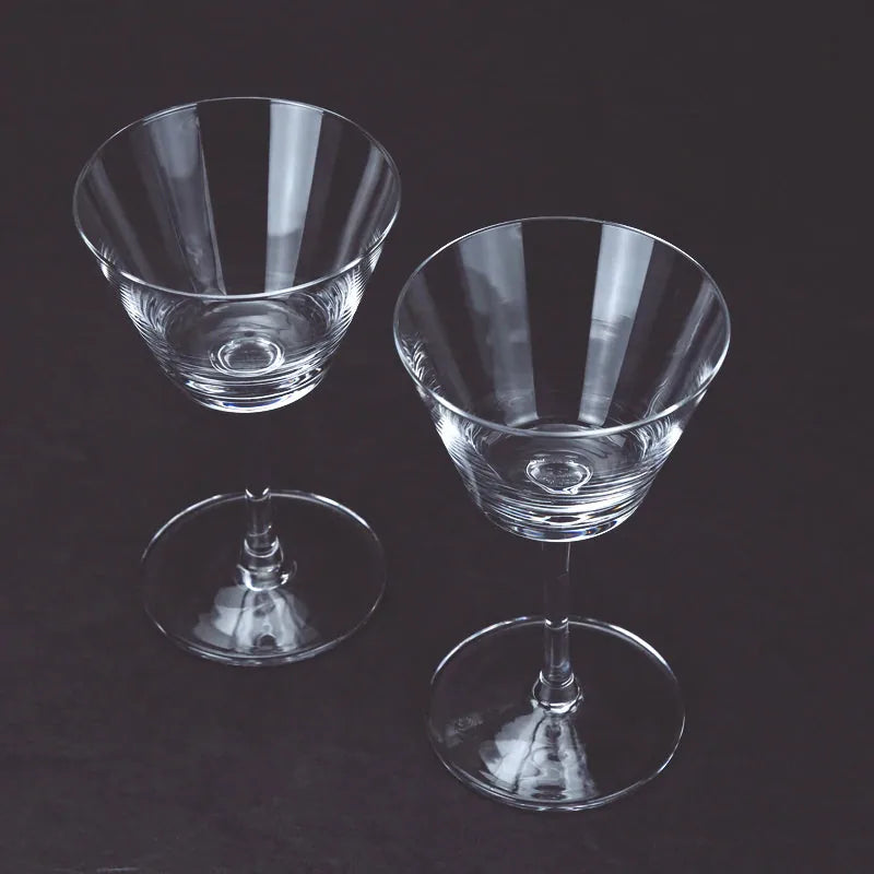 Deux verres à cocktail coupe vintage vides, disposés côte à côte sur fond noir.