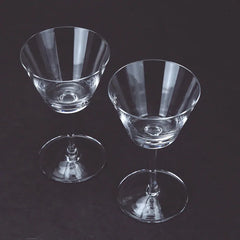 Deux verres à cocktail coupe vintage vides, disposés côte à côte sur fond noir.