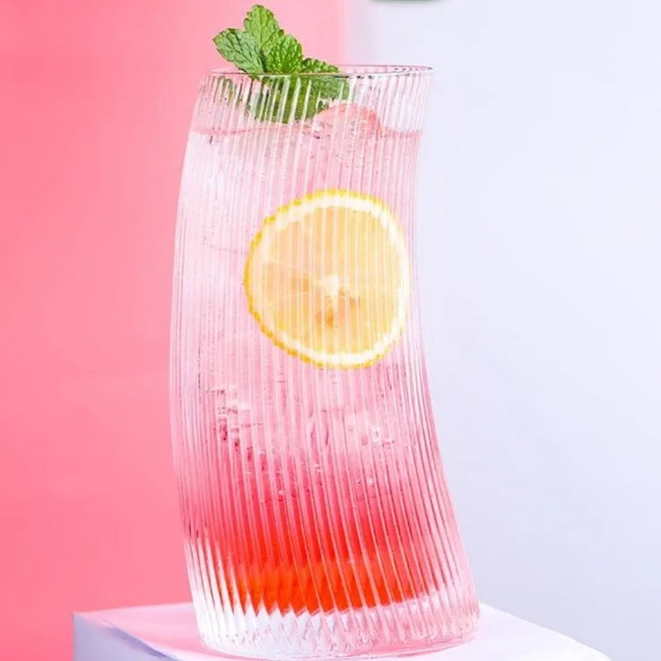Verre à cocktail courbé contenant un cocktail rose garni d'une rondelle de citron et de menthe fraîche, sur fond rose