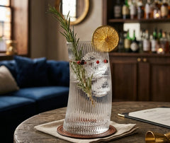 Verre à cocktail courbé rempli d'un gin tonic garni de romarin et d'une rondelle d'orange séchée, posé sur une table dans un bar cosy