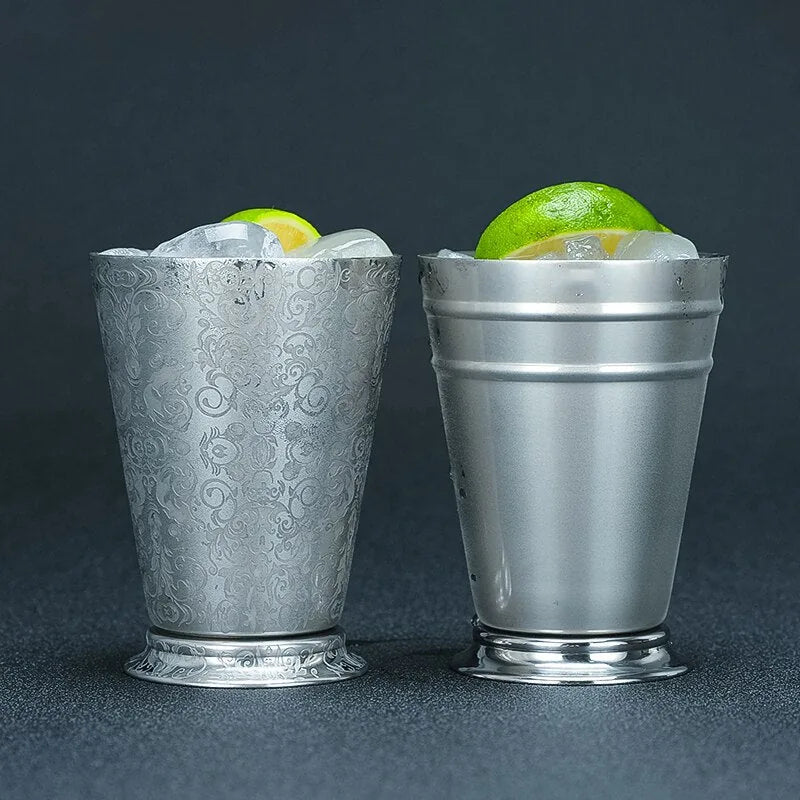 Les deux finitions du verre à cocktail Gourmandise, Cachemire à motif gravé et Moderne uni, présentées côte à côte remplies de glace et de citron, sur fond gris foncé.
