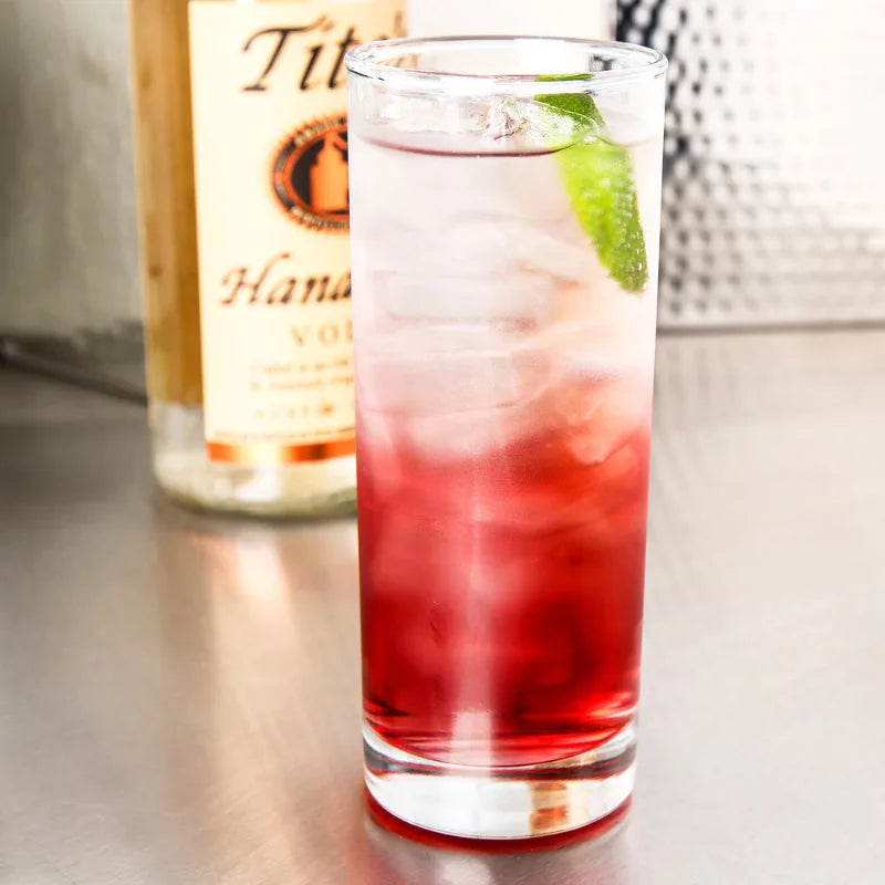Verre à cocktail long drink avec boisson en dégradé rouge et citron vert, bouteille de vodka Tito's en arrière-plan