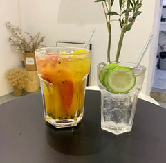 Deux verres à cocktail Mojito XL sur table noire, l'un avec jus de fruits rouges et pamplemousse, l'autre avec eau pétillante au concombre et citron vert