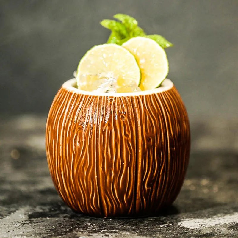 Verre à cocktail noix de coco garni de rondelles de citron vert et de feuilles de menthe fraîche, posé sur fond gris