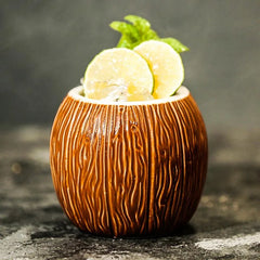 Verre à cocktail noix de coco garni de rondelles de citron vert et de feuilles de menthe fraîche, posé sur fond gris