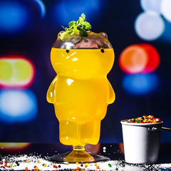 Verre ours rempli d'un cocktail jaune garni de menthe fraîche et de myrtilles, ambiance nocturne colorée
