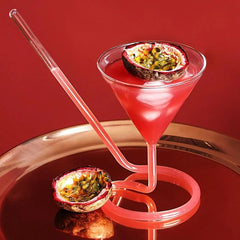 Verre à cocktail avec paille intégrée bicolore bleu et rose, rempli d'un cocktail orange, sur fond noir