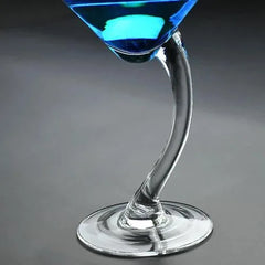 Gros plan incliné sur un verre à cocktail bleu avec un pied courbé en verre transparent.
