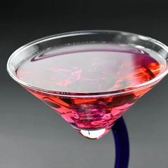 Gros plan sur le rebord du verre à cocktail rempli d'un cocktail rouge et d'un glaçon rose.