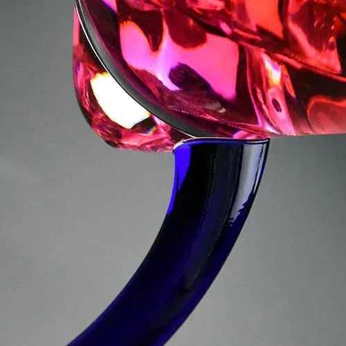 Gros plan macro sur la jonction entre la coupe et le pied courbé bleu cobalt du verre à cocktail, avec un cocktail rose.
