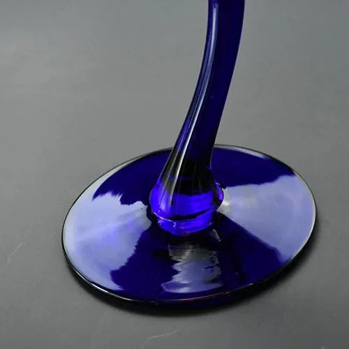 Macro photo du pied courbé en verre bleu cobalt du verre à cocktail, posé sur sa base ovale.