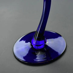 Macro photo du pied courbé en verre bleu cobalt du verre à cocktail, posé sur sa base ovale.
