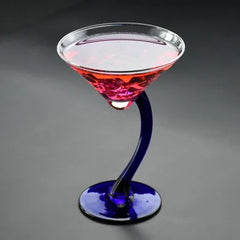 Verre à cocktail pied courbé rempli d'un cocktail rouge, avec un pied incurvé en verre bleu cobalt, sur fond gris.