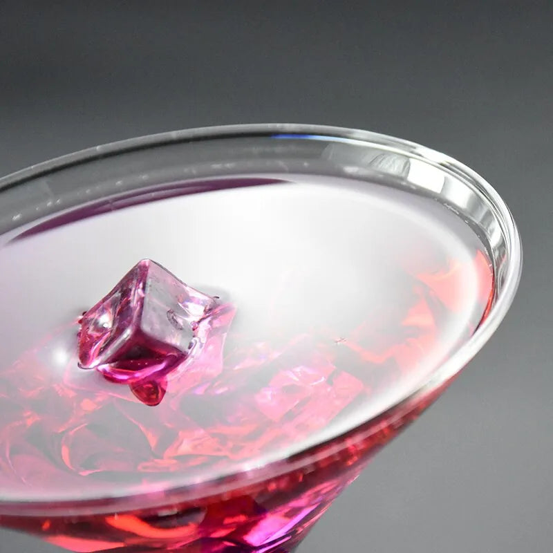 Vue plongeante sur le rebord du verre à cocktail avec un cocktail rouge et un glaçon rose translucide.