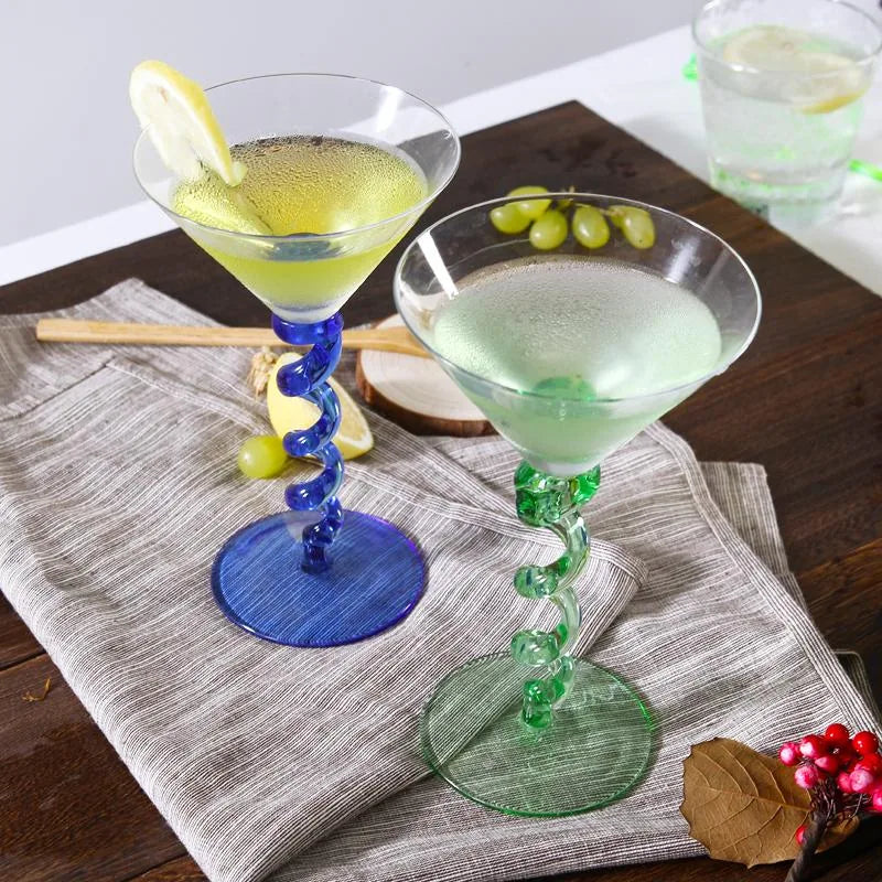 Les verres à pied torsadé bleu et vert garnis de rondelles de citron et de grains de raisin, posés sur une nappe en tissu gris.