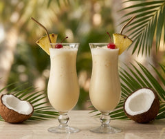 Deux verres de Piña Colada dans un décor tropical avec noix de coco et feuilles de palmier