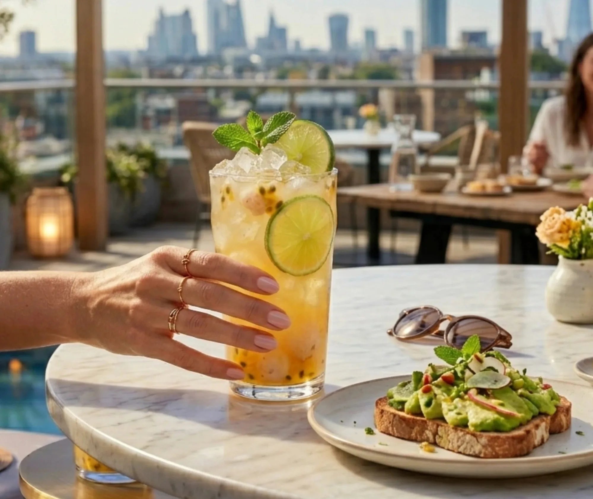 Grand verre à punch cocktail au fruit de la passion et citron vert, tenu à la main sur une terrasse avec vue sur la ville