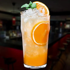 Grand verre à punch cocktail orange avec glaçons, tranche d'orange et menthe fraîche, posé sur un bar