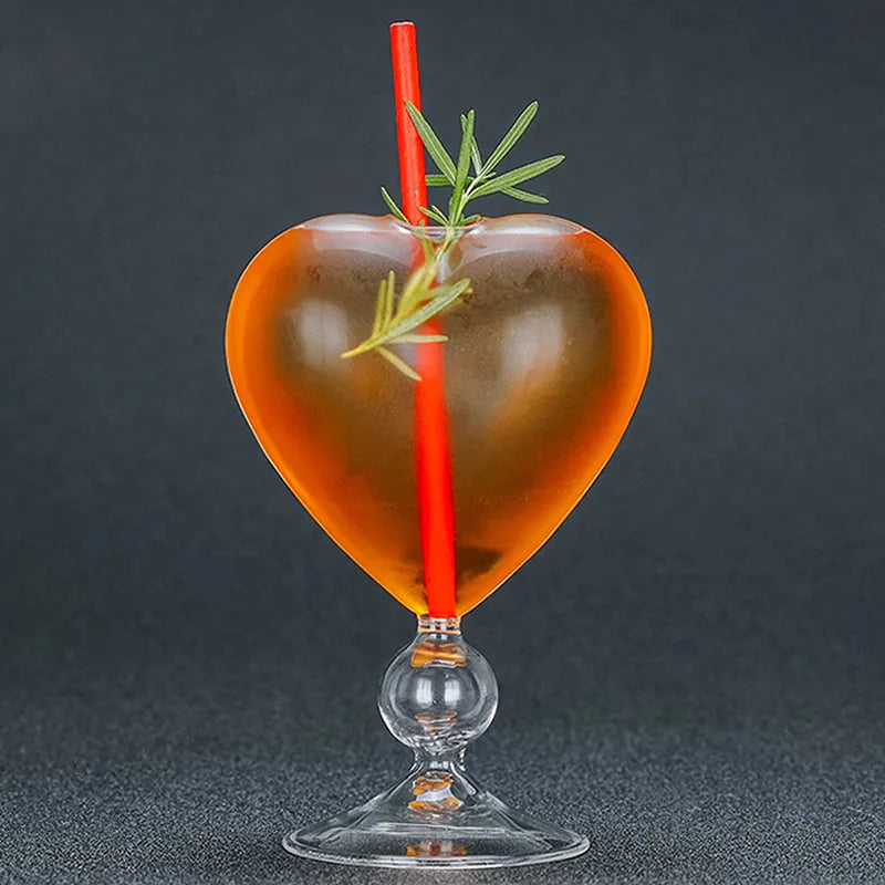 Verre à cocktail cœur ambré garni d'un brin de romarin, photographié sur fond noir
