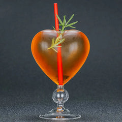 Verre à cocktail cœur ambré garni d'un brin de romarin, photographié sur fond noir