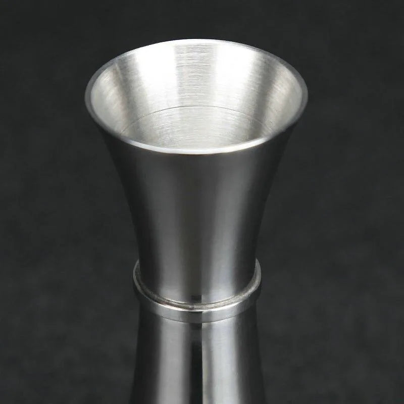 Gros plan sur l'embouchure évasée du verre doseur à cocktail, finition brossée sur fond sombre.