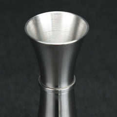 Gros plan sur l'embouchure évasée du verre doseur à cocktail, finition brossée sur fond sombre.