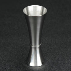 Verre doseur à cocktail en acier inoxydable, vue de profil complète sur fond noir.