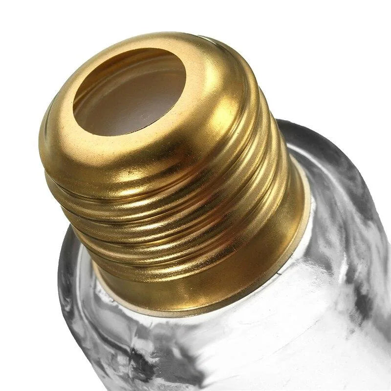 Gros plan sur le bouchon doré vissé du verre à cocktail en forme d'ampoule, mettant en valeur le filetage métallique et le verre transparent.