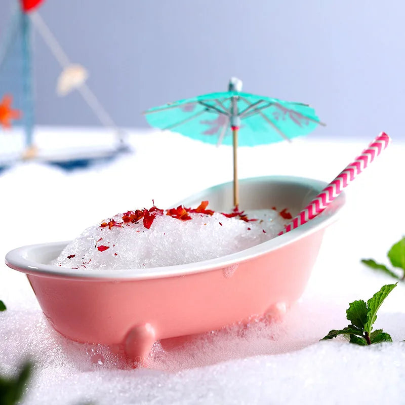 Verre en forme de baignoire rose rempli de glace pilée, décoré d'un parasol de cocktail turquoise et d'une paille rayée rose