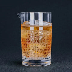 Verre à mélange rempli de glaçons et de cocktail ambré, photographié en gros plan sur fond noir.