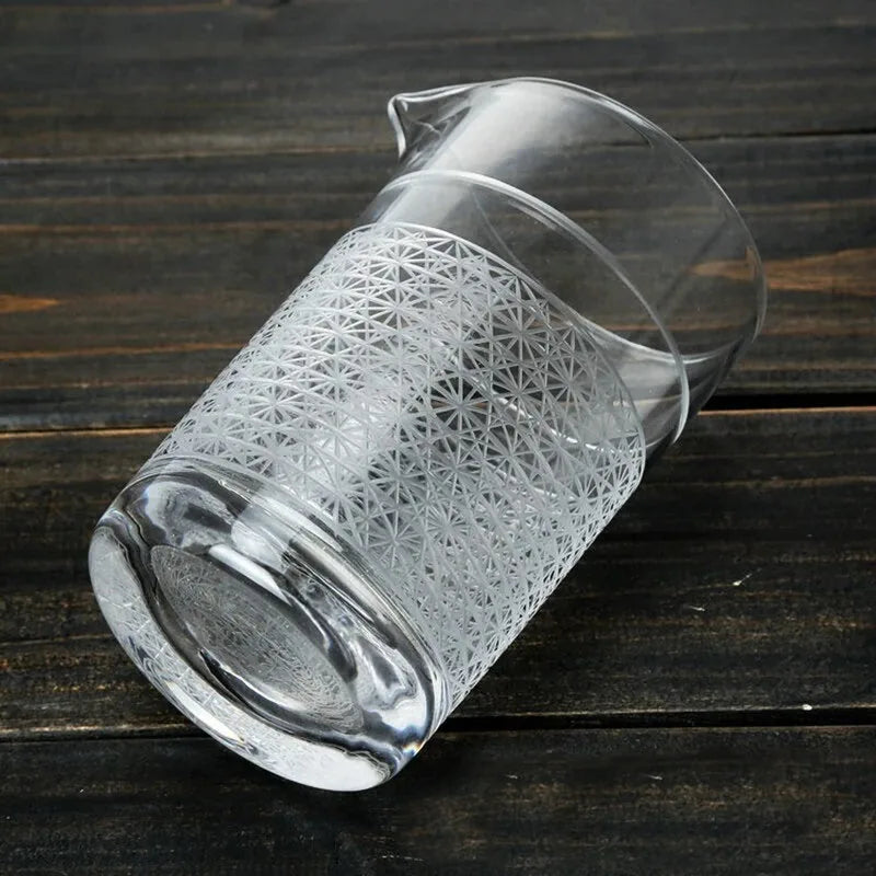 Verre à mélange incliné posé sur une table en bois sombre, mettant en valeur son motif gravé et son bec verseur.